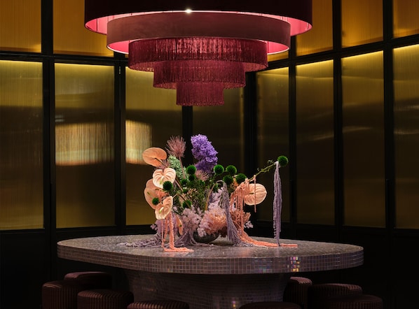 A round table with a floral centerpiece, a hanging light fixture, and a view of a building with large windows. - Naumi Studio Wellington (Wellington)