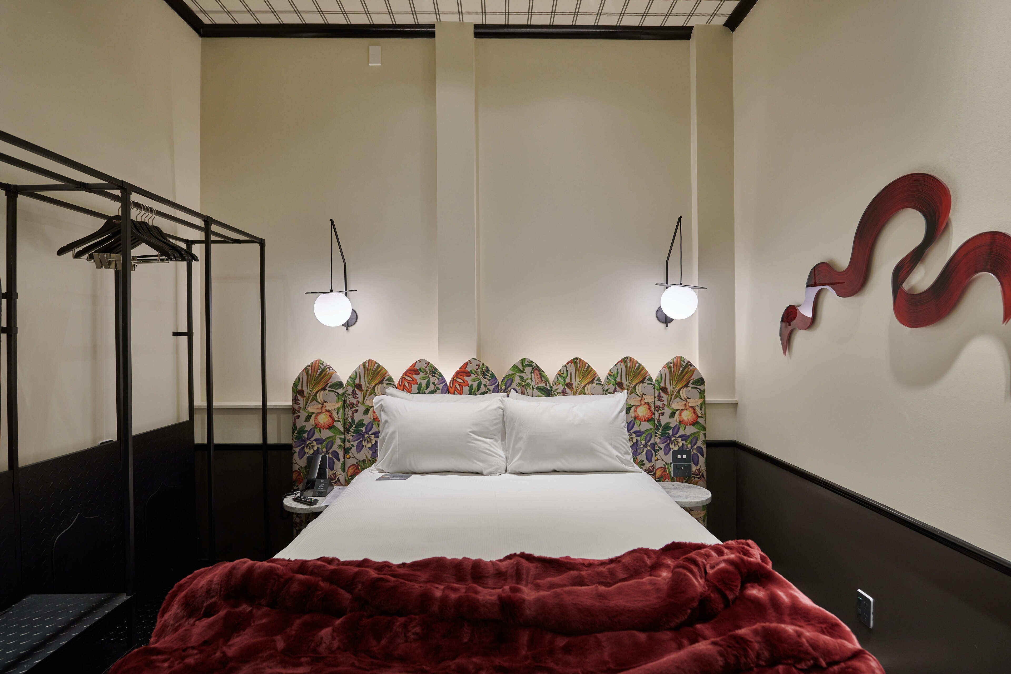 Ein Hotelzimmer mit einem Bett, einer roten Decke, einem Wandbild und einem Kleiderhaken.