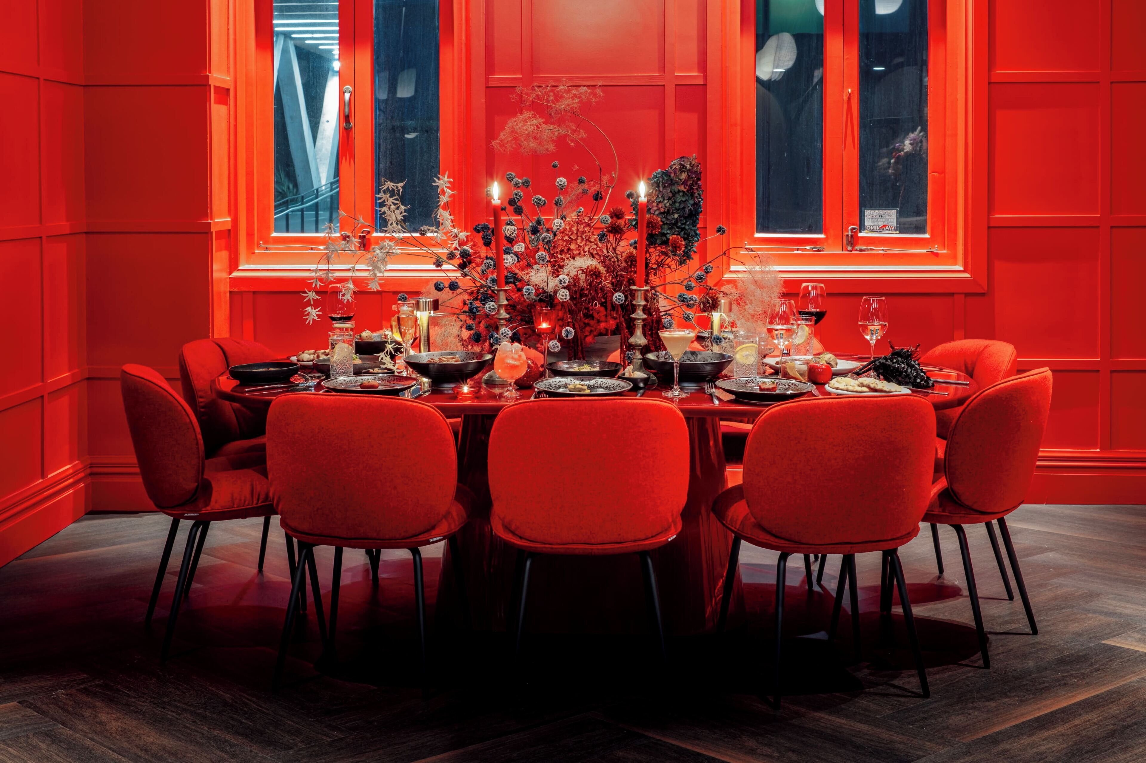 A dining area with a red-themed decor, featuring a table set for six with red chairs, candles, and a floral centerpiece.