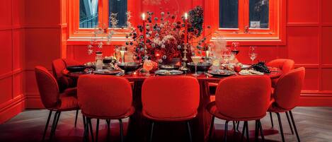 A dining area with a red-themed decor, featuring a table set for six with red chairs, candles, and a floral centerpiece.