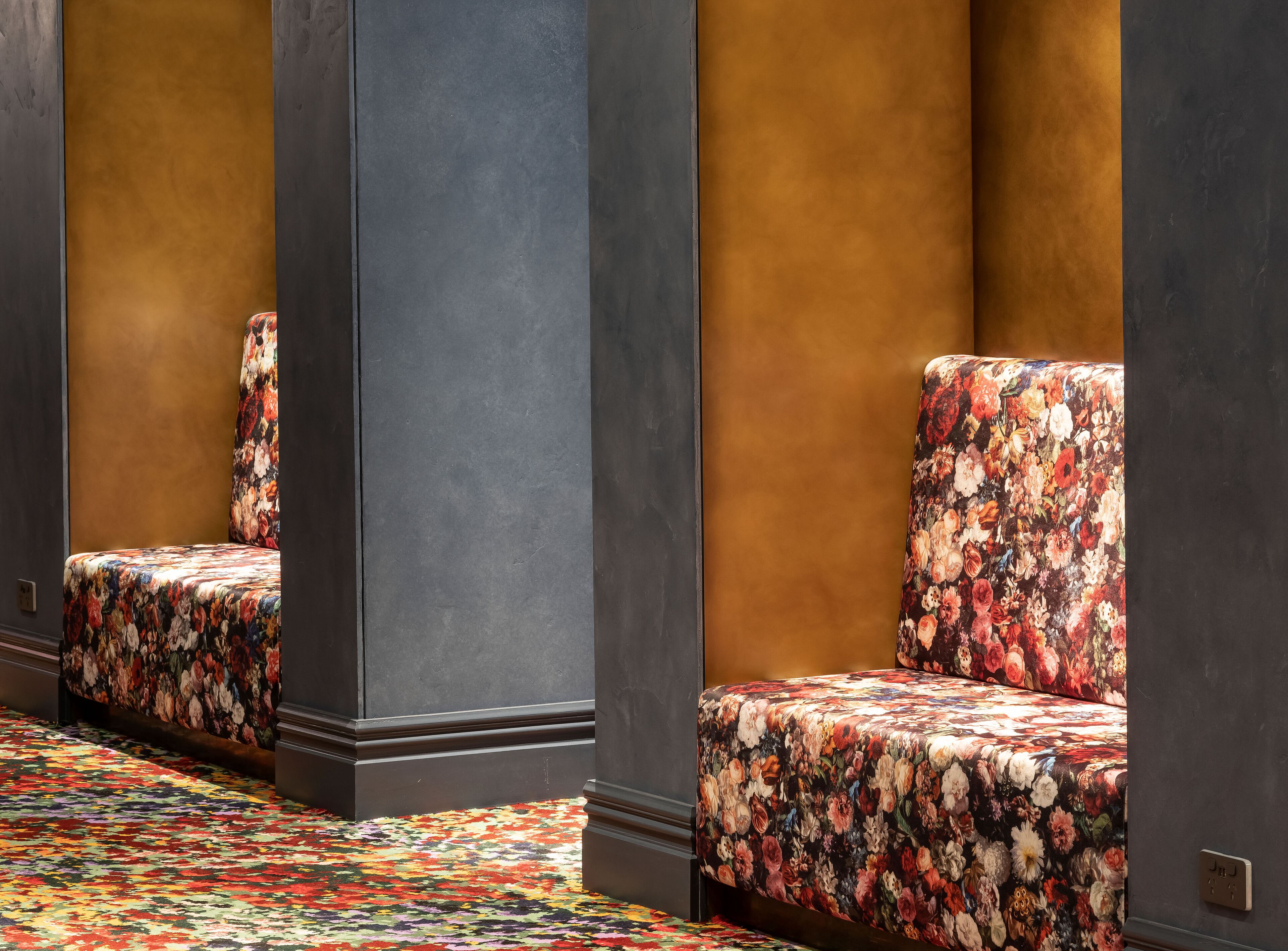 A hotel room with a floral-patterned sofa, a patterned carpet, and dark walls.