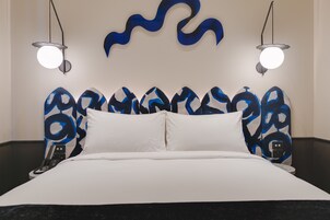 Una habitación de hotel moderna con una cama grande, ropa de cama blanca y un original cabecero abstracto azul.