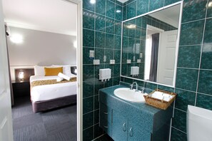 Enjoy a restful night's sleep in this stylish room featuring a comfortable bed and a modern bathroom with a large mirror and sink.