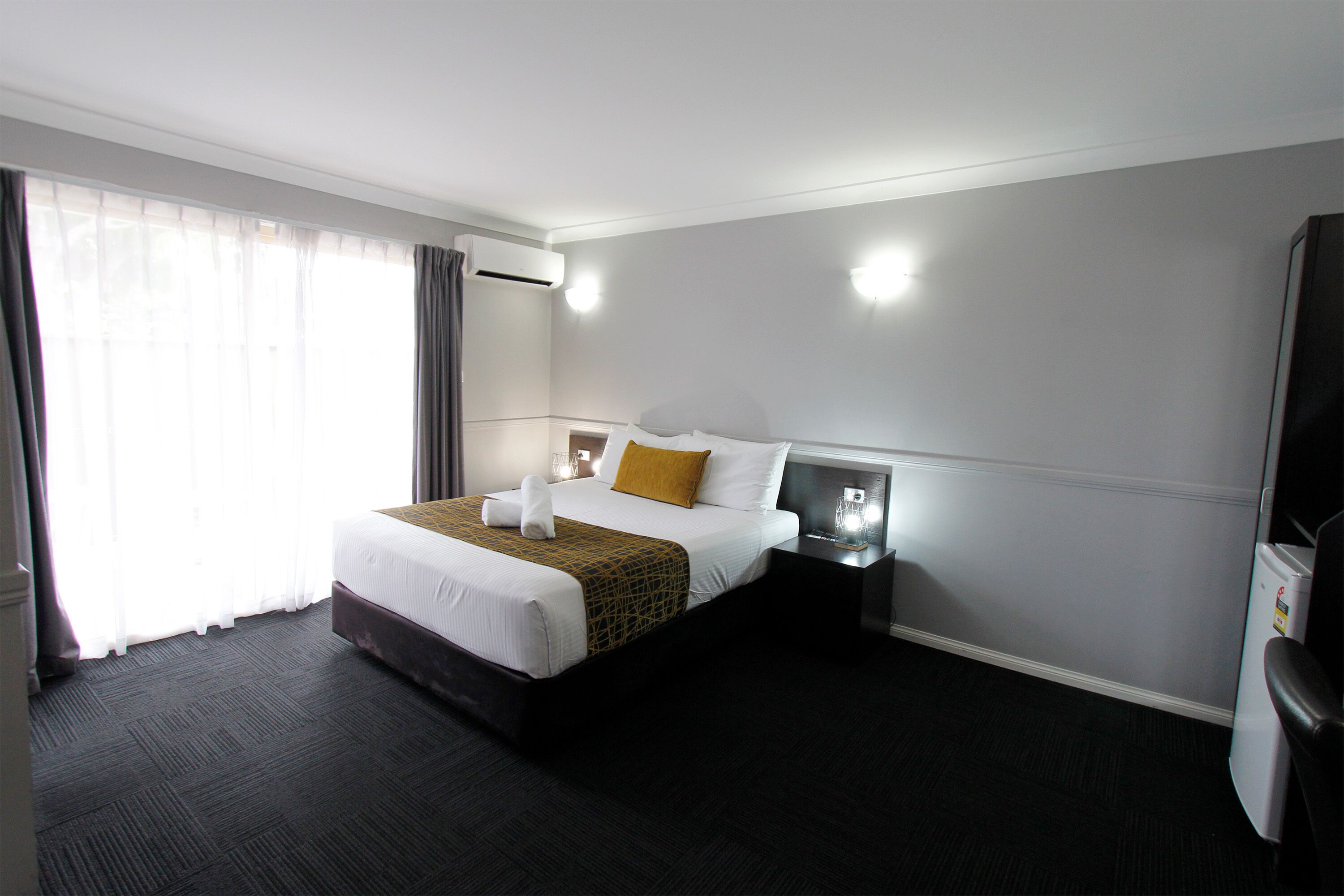 A hotel room with a large bed, a bedside table, an air conditioning unit, and a television.