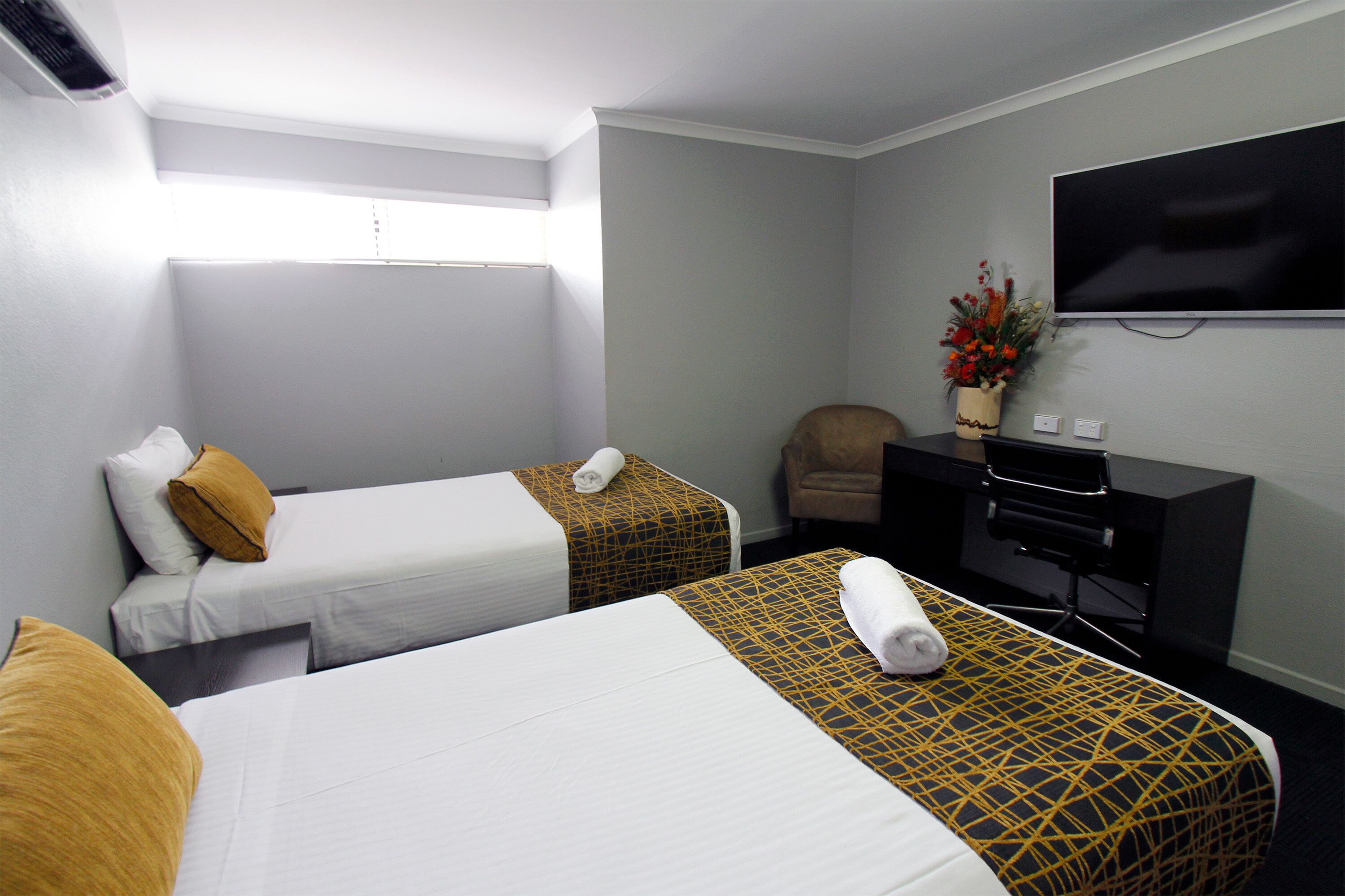 Quarto de hotel com duas camas, televisão, escrivaninha e uma cadeira.
