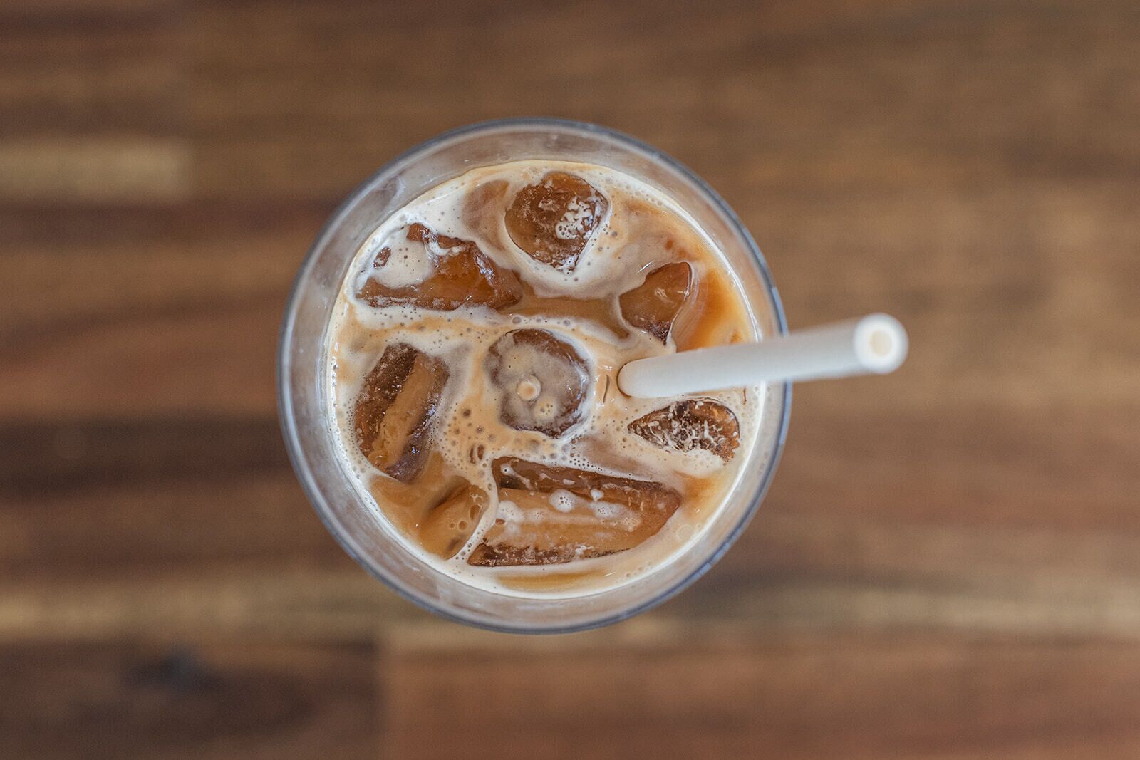 A glass of iced coffee with ice cubes and a white straw on a wooden surface.