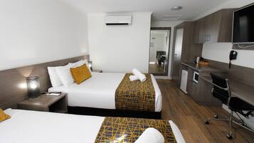 A hotel room with two beds, a desk, a chair, a TV, and a kitchenette.