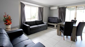 Uma sala de estar moderna com um sofá cinzento, uma mesa de jantar com cadeiras, uma televisão de tela plana e uma janela com cortinas.
