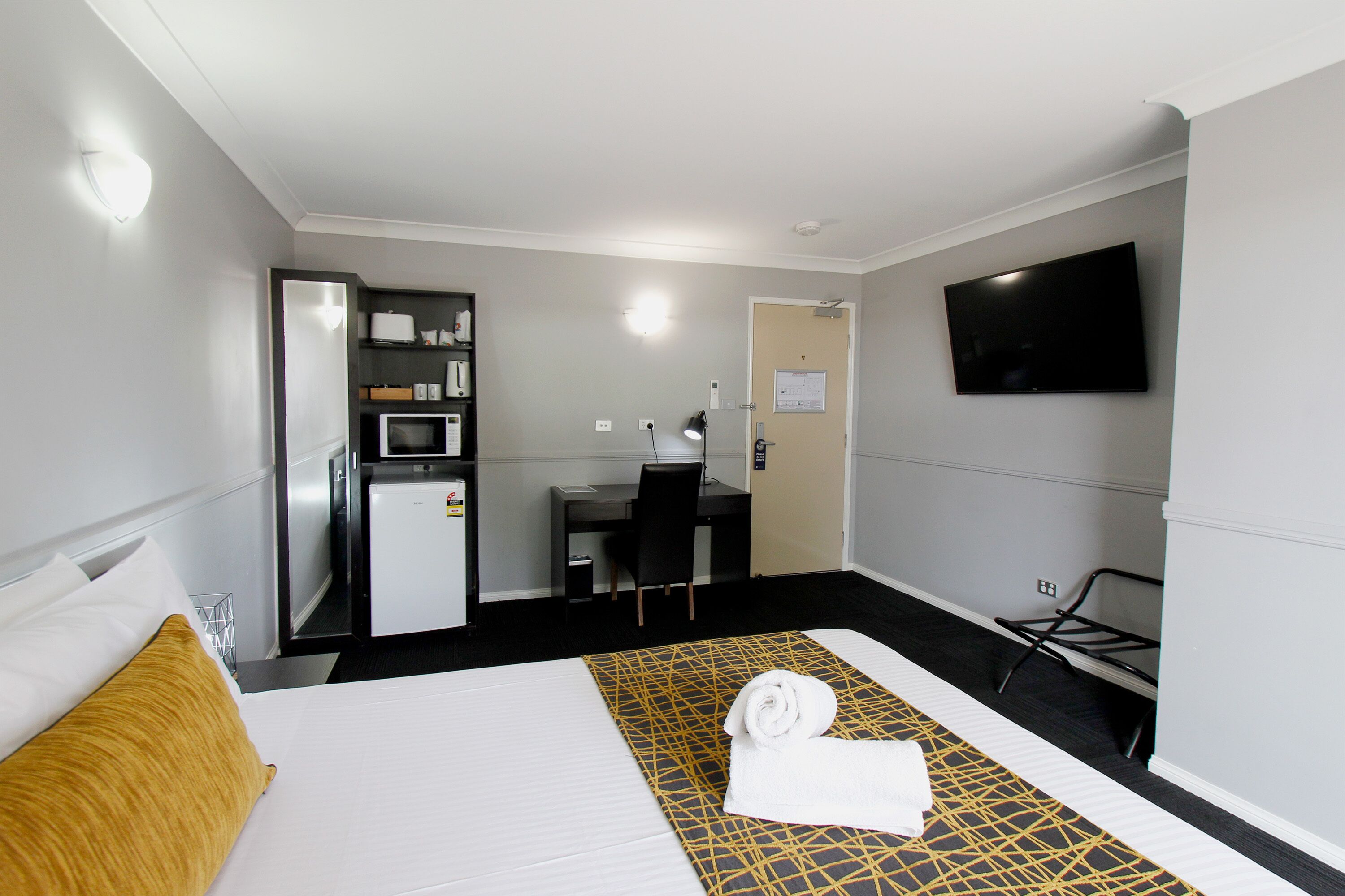 Una habitación de hotel con cama, escritorio, silla, televisor y microondas.