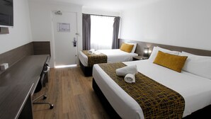 Quarto de hotel com duas camas, uma escrivaninha e uma janela com cortinas.