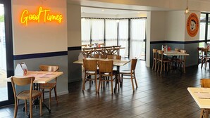 Interior de restaurante com mesas e cadeiras de madeira, um letreiro de neon 'Good Times' e o logotipo 'Buddy Boy Kitchen' na parede.