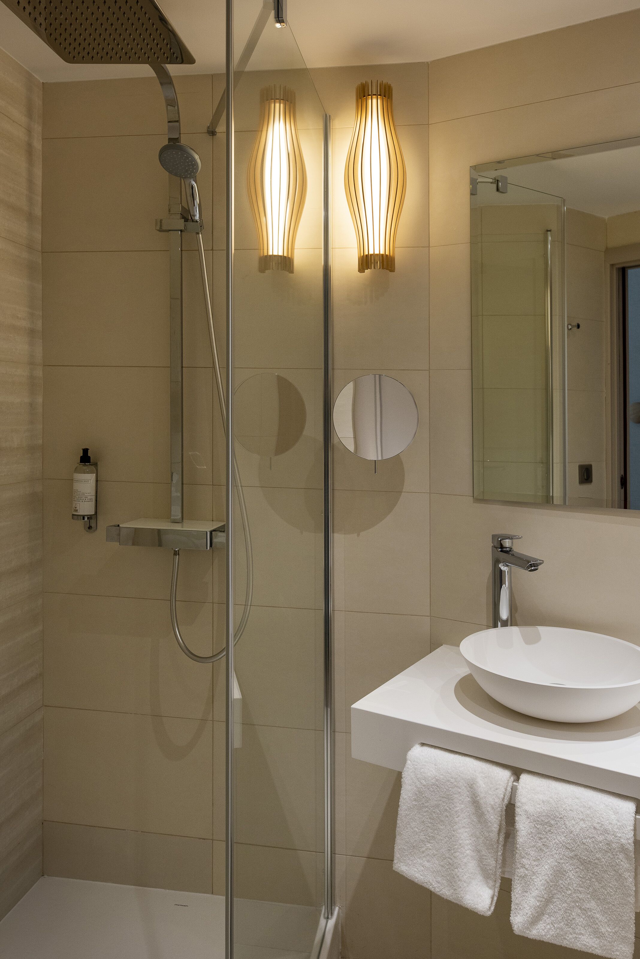 A modern bathroom with a glass-enclosed shower, a white sink, and a mirror above it.