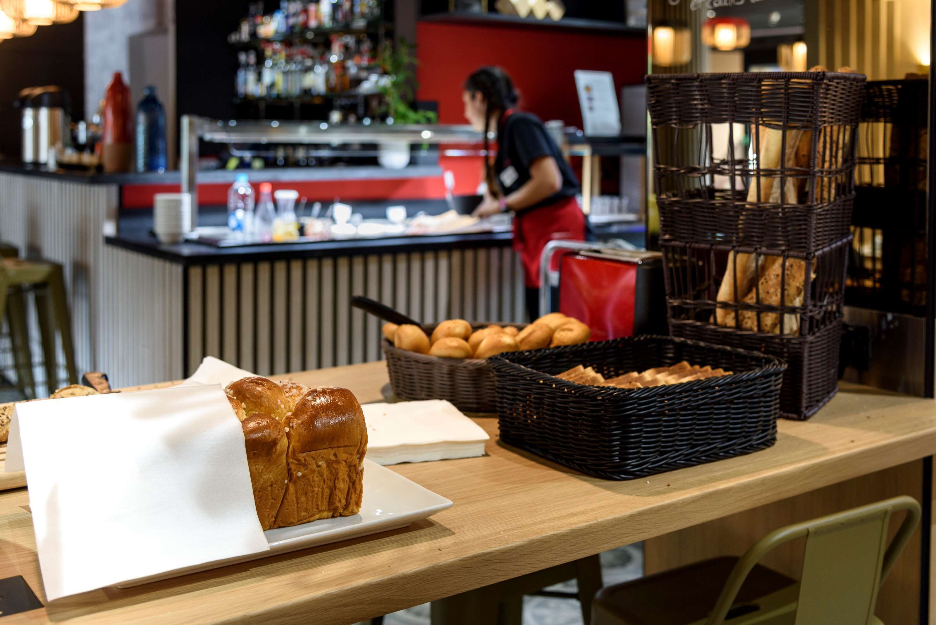 Un comptoir de boulangerie avec du pain et des pâtisseries, un bar à l’arrière-plan et une personne qui travaille derrière le comptoir.