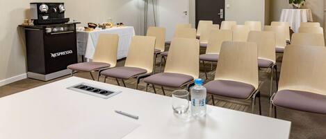 Una sala de conferencias con una mesa blanca, sillas, una máquina de café Nespresso, una botella de agua y una puerta de servicio.