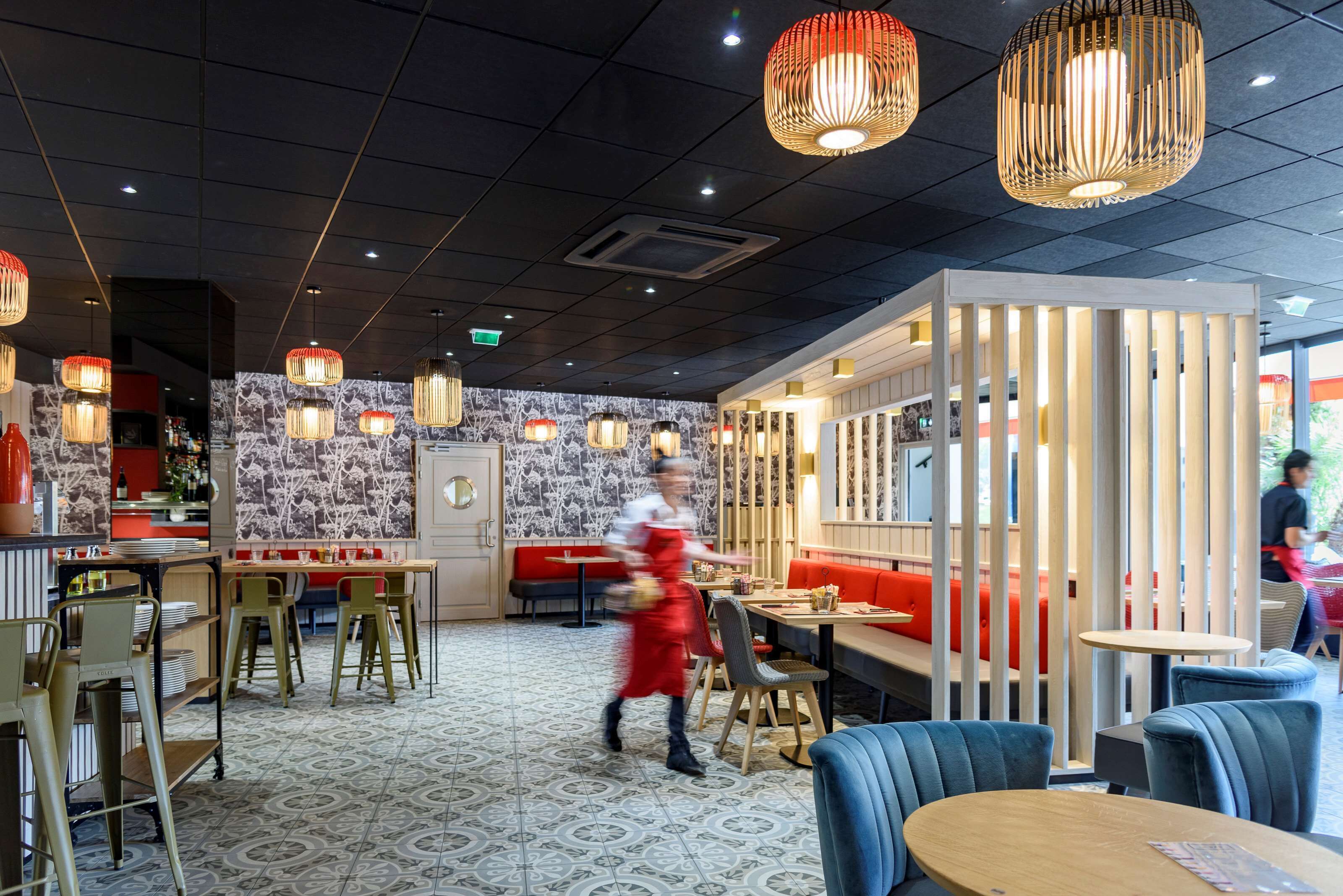 Een restaurantinterieur met een modern design, met een patroon vloer, rode en blauwe zitplaatsen en hangende pendellampen.