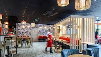 Interior de restaurante con diseño moderno, que presenta un suelo estampado, asientos en rojo y azul, y lámparas colgantes.