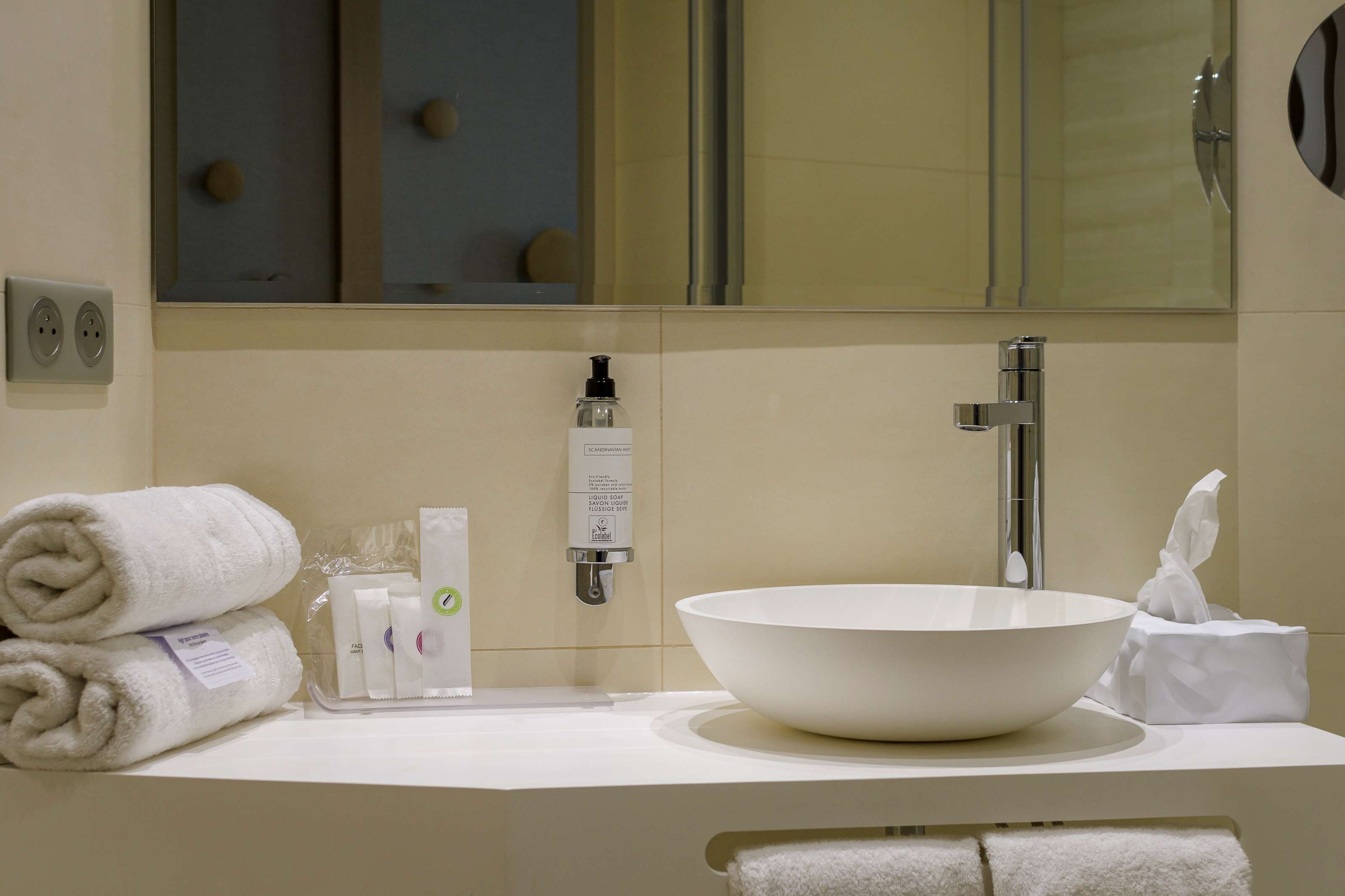 A modern bathroom with a large white sink, a mirror, and neatly folded towels.