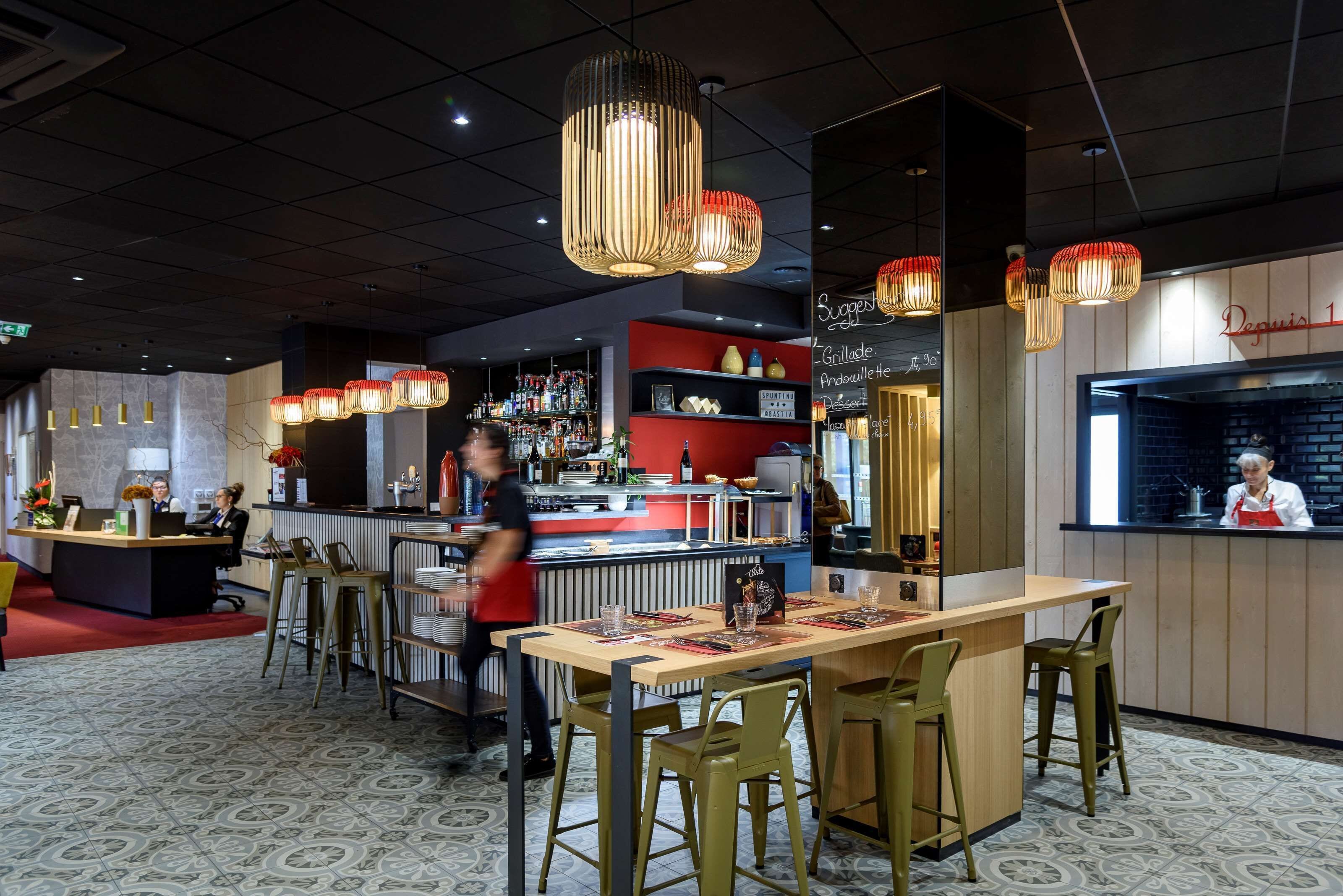 A modern restaurant interior with a bar area, seating, and a visible kitchen.
