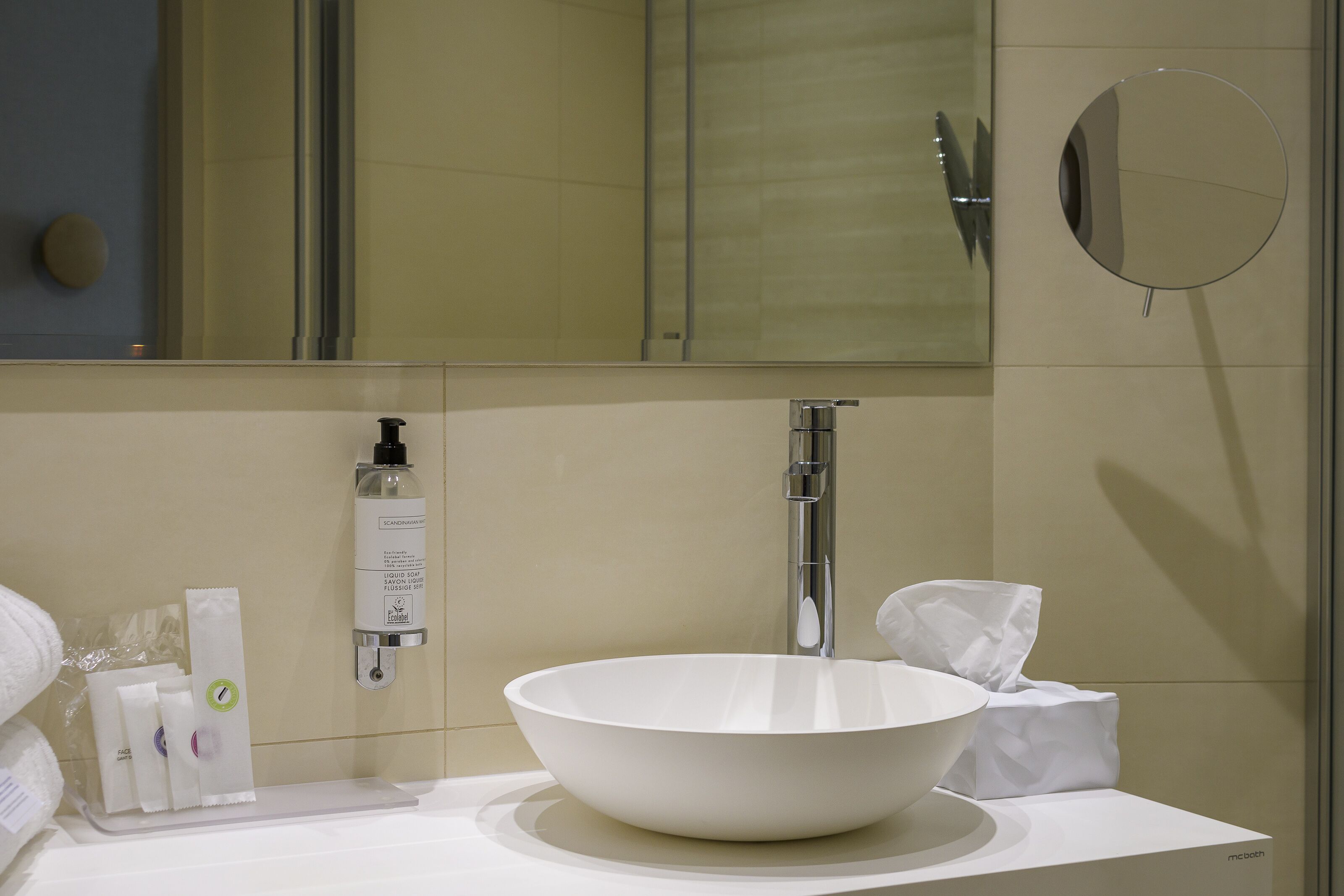 A modern bathroom with a white sink, a mirror, and toiletries on the counter.