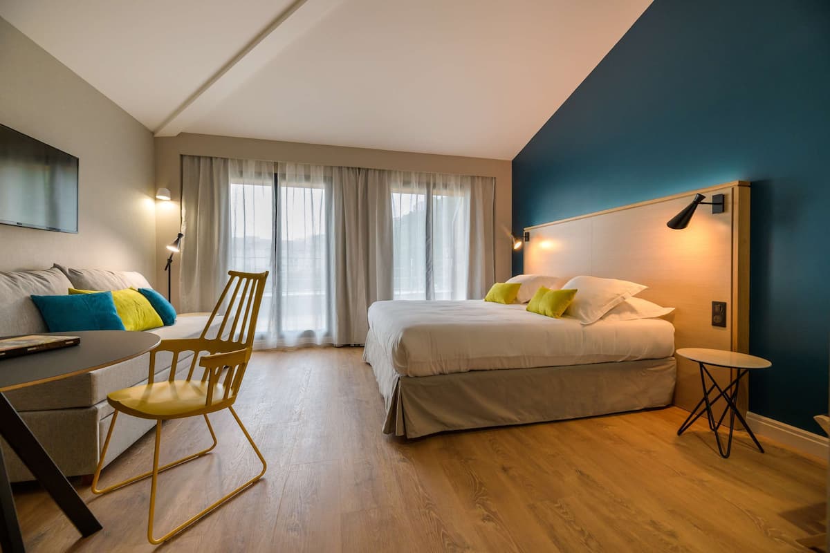 A modern hotel room with a bed, a desk, a chair, and a small table.