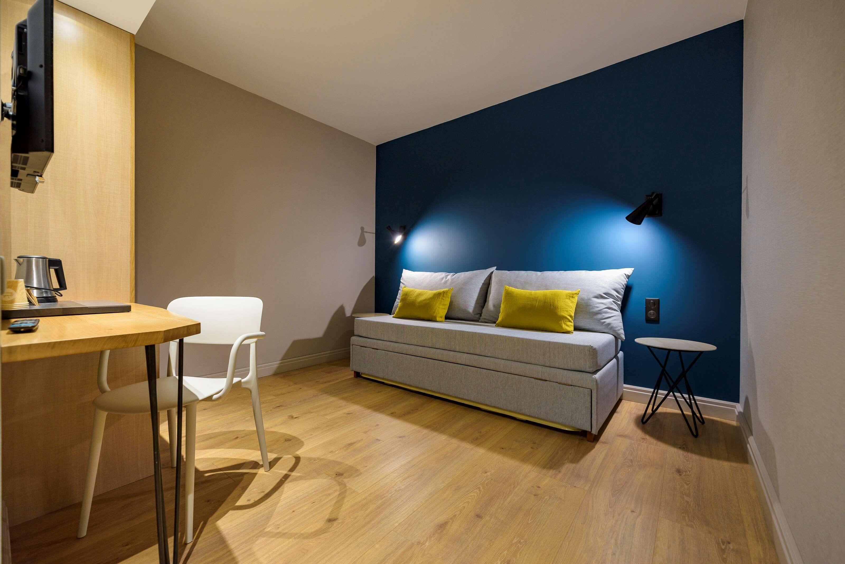 A modern room with a grey sofa, a small round table, a white chair, and a wooden desk.