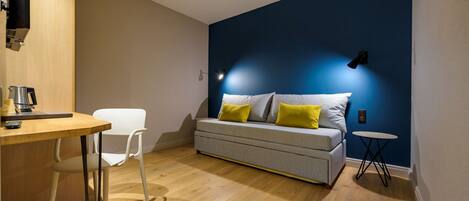 A modern room with a grey sofa, a small round table, a white chair, and a wooden desk.