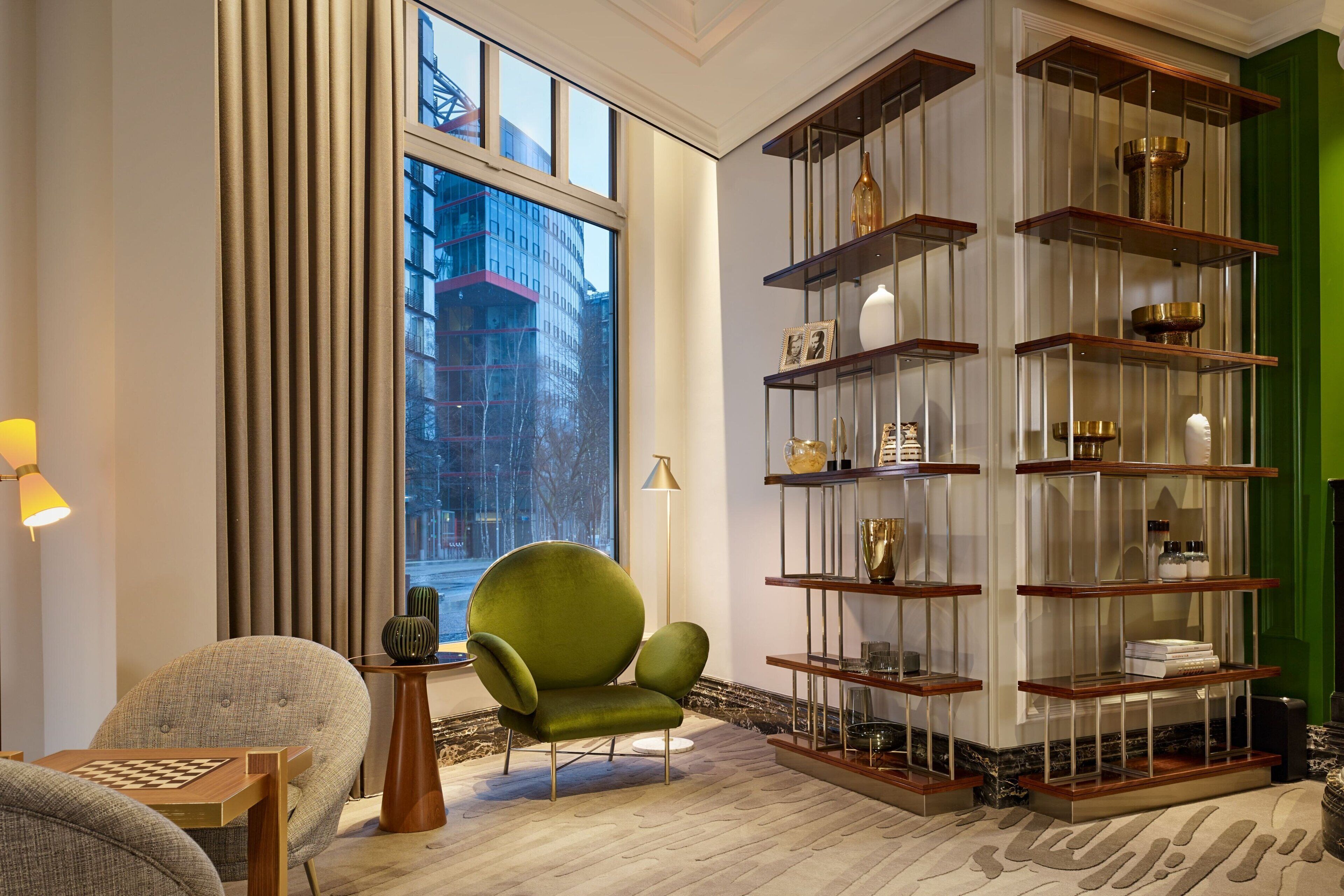 A modern living room with a large window, a green armchair, a wooden coffee table, and a glass display unit with decorative items.