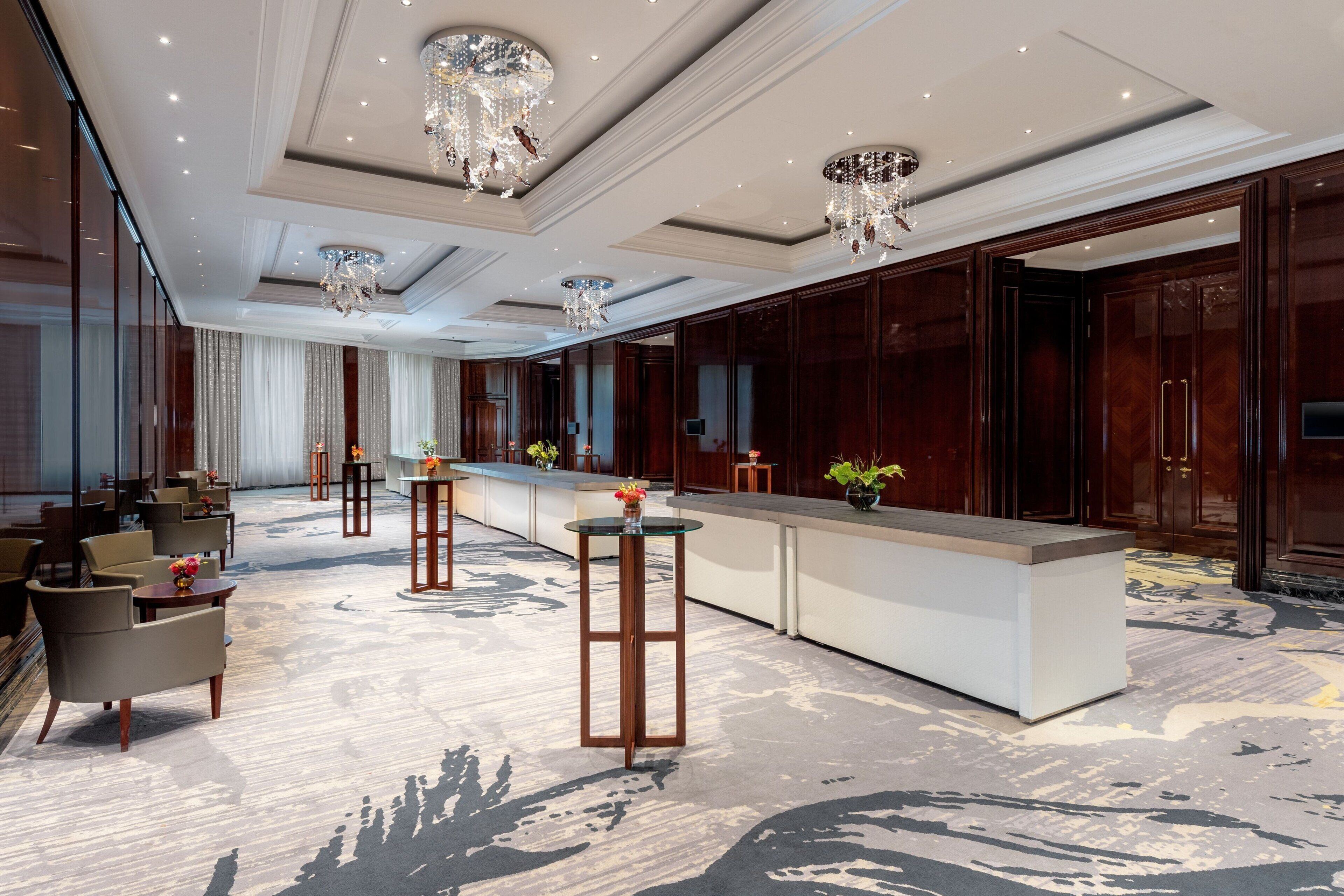 Un hall d’hôtel spacieux avec un bar central, des espaces aménagés pour s’asseoir et un éclairage décoratif.