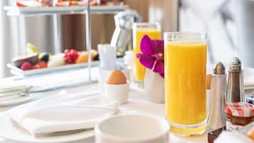 Una presentación para el desayuno con una bandeja de frutas y quesos de tres niveles, un vaso de zumo de naranja, una taza de café y un bol pequeño de huevos.