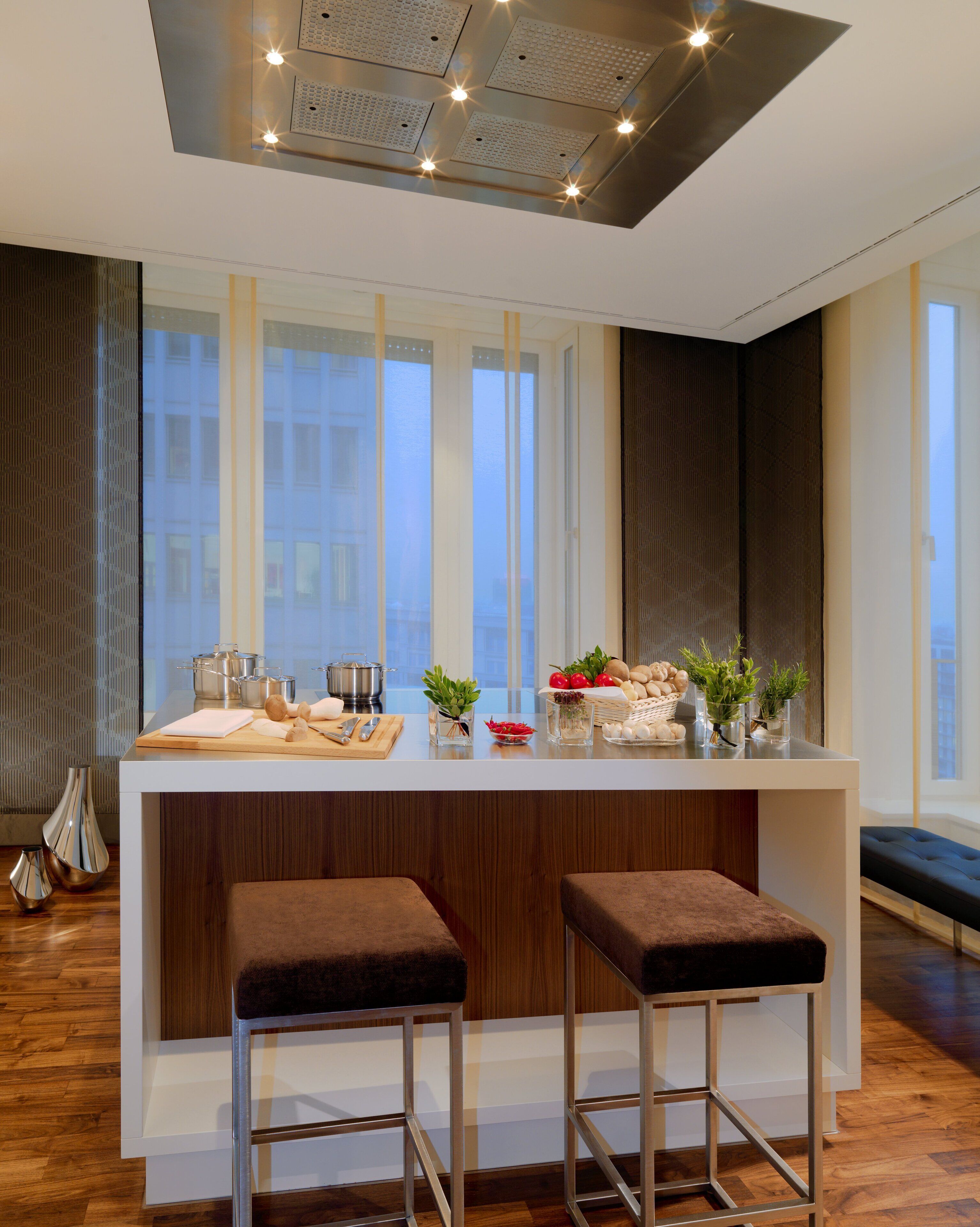 A modern kitchen with a central island, bar stools, and large windows.