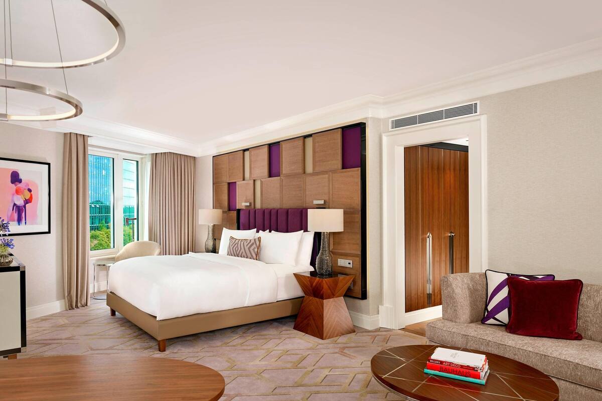Habitación de hotel con una cama grande, un sofá, una mesita de centro y un escritorio con lámpara.