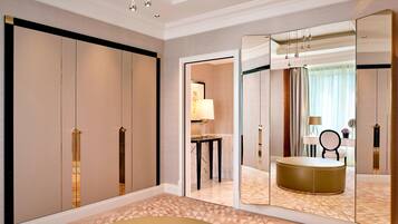 A hotel room with a large mirror, a round ottoman, a small table with a lamp, and a view of a bathroom through an open door.