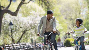 Dues persones van en bicicleta per un parc amb bancs i arbres.