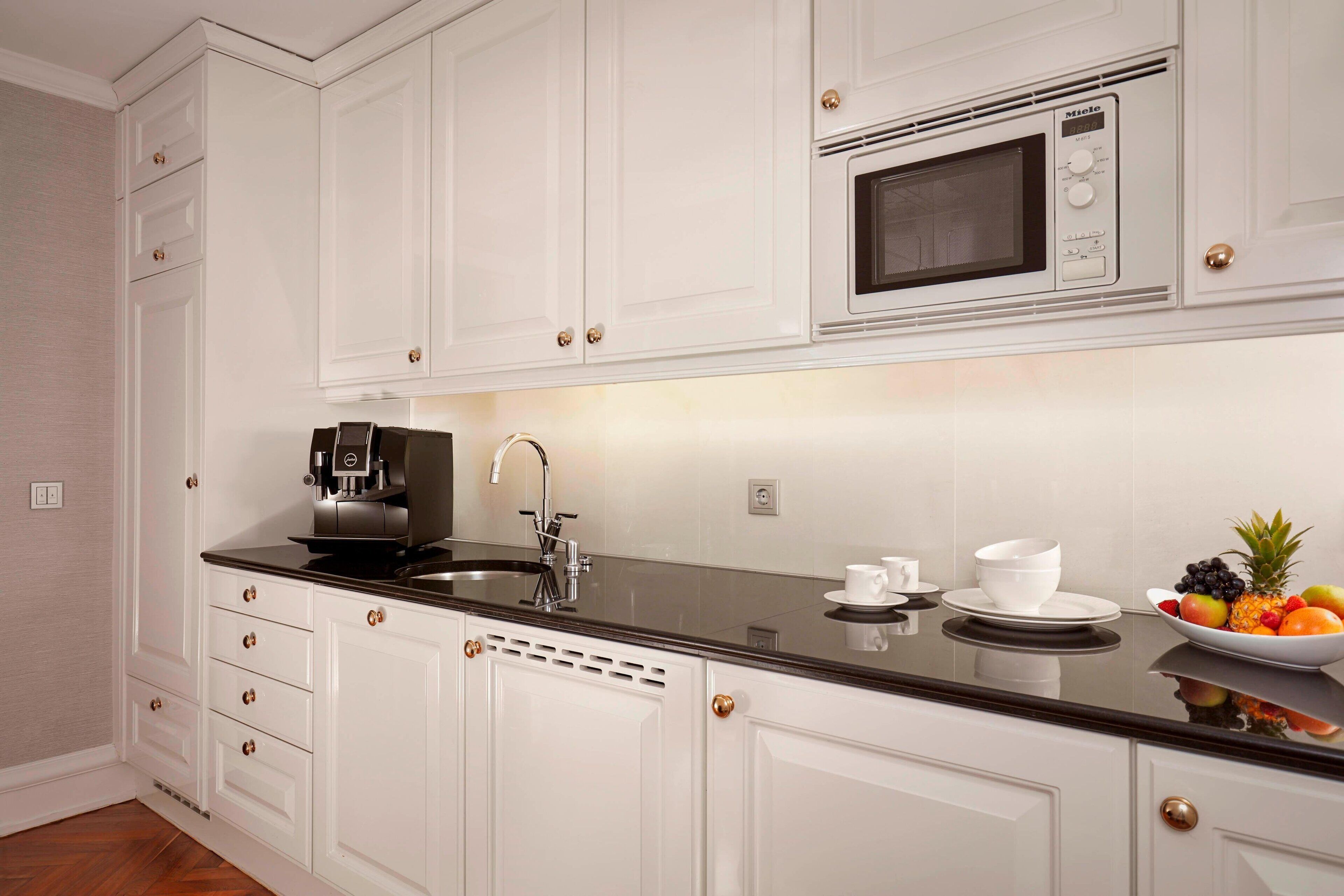 A modern kitchen with white cabinetry, a black countertop, a built-in microwave, a coffee machine, and a fruit bowl.