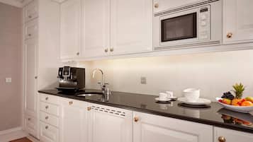 A modern kitchen with white cabinetry, a black countertop, a built-in microwave, a coffee machine, and a fruit bowl.