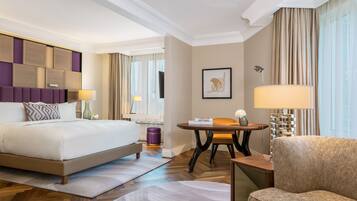 Une chambre d’hôtel avec un grand lit, un coin salon avec une table et une chaise, et une vue sur la ville par la fenêtre.