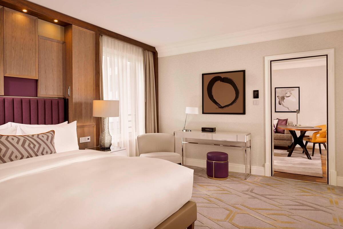 Habitación de hotel con una cama grande, un escritorio, una silla, una mesita pequeña, una lámpara y una obra de arte colgada en la pared.