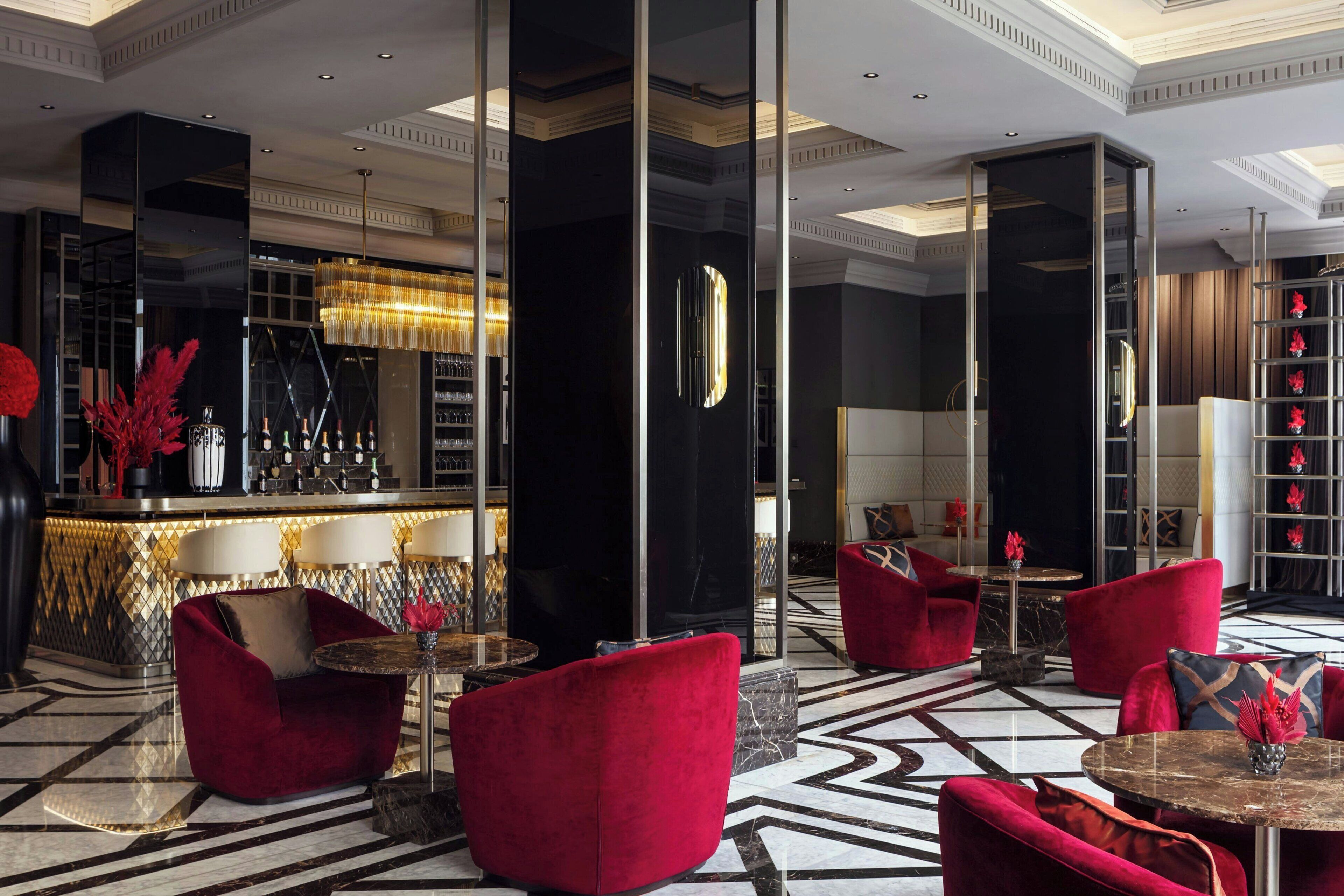 Eine Lobby mit Barbereich, roten Polstersesseln, Marmorböden und einem modernen Kronleuchter.