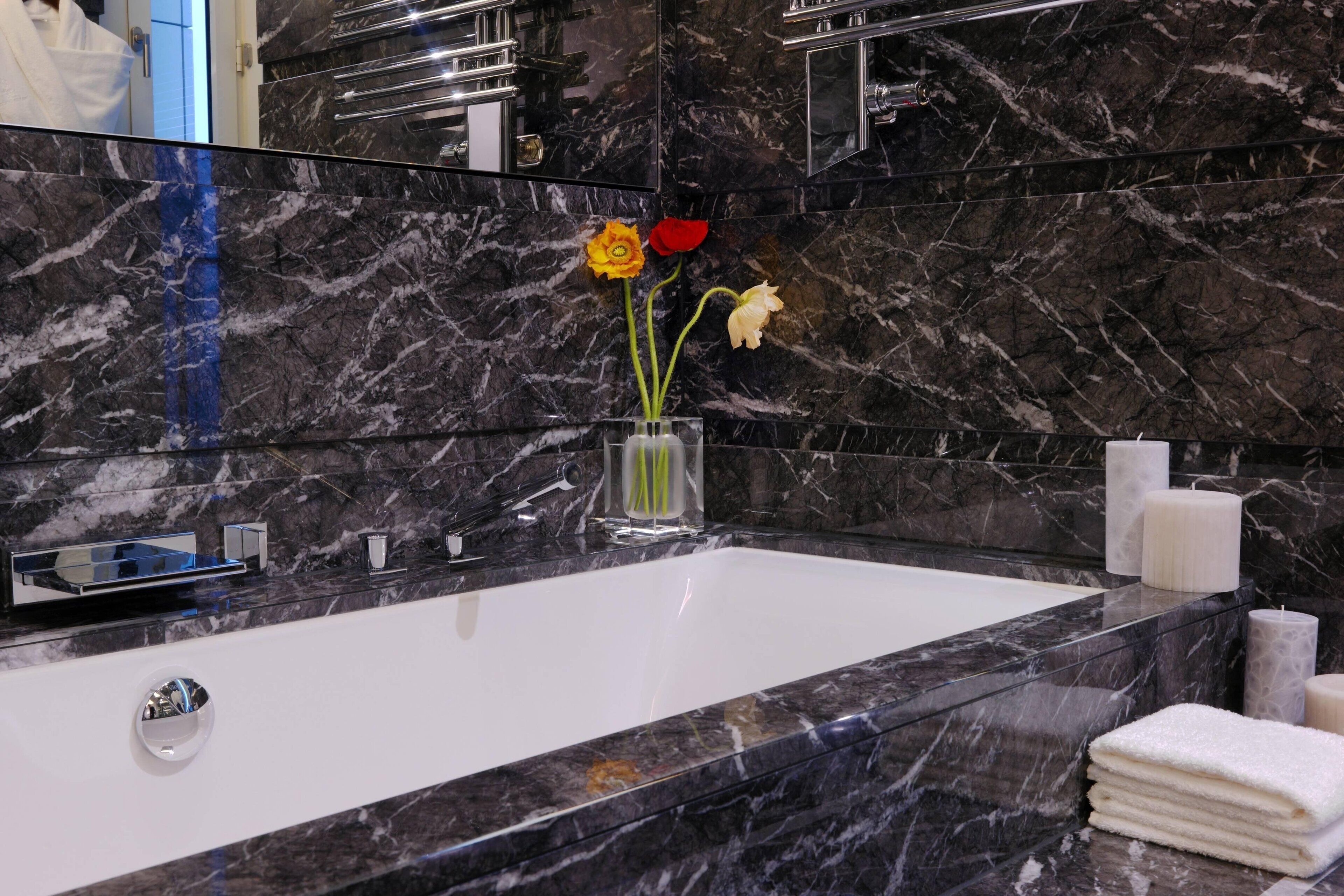 Une salle de bain moderne avec un lavabo en marbre, une grande baignoire et un vase rempli de fleurs.