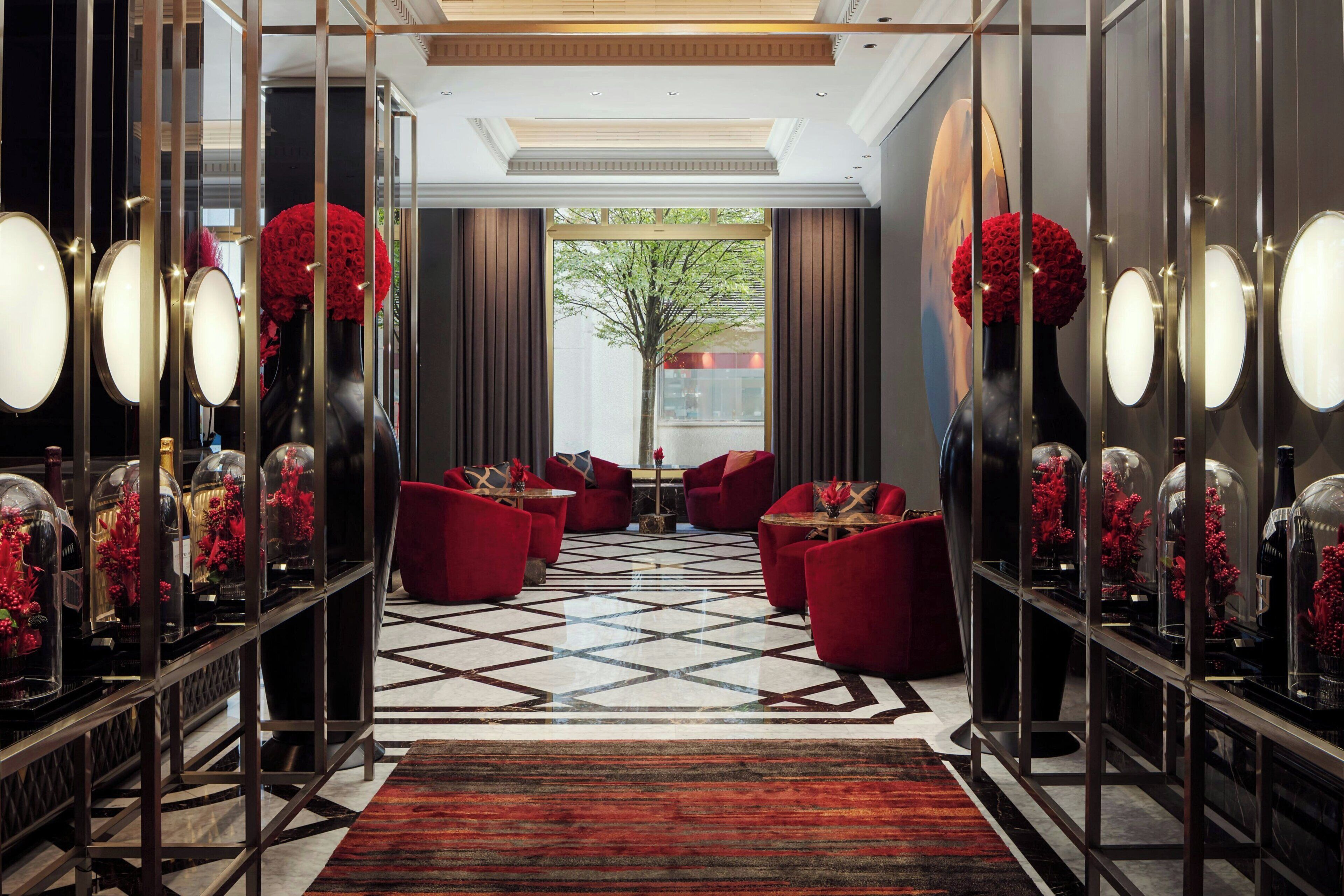 A hotel lobby with a geometric patterned floor, red seating, and glass display cases with red flowers.