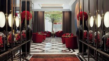 A hotel lobby with a geometric patterned floor, red seating, and glass display cases with red flowers.