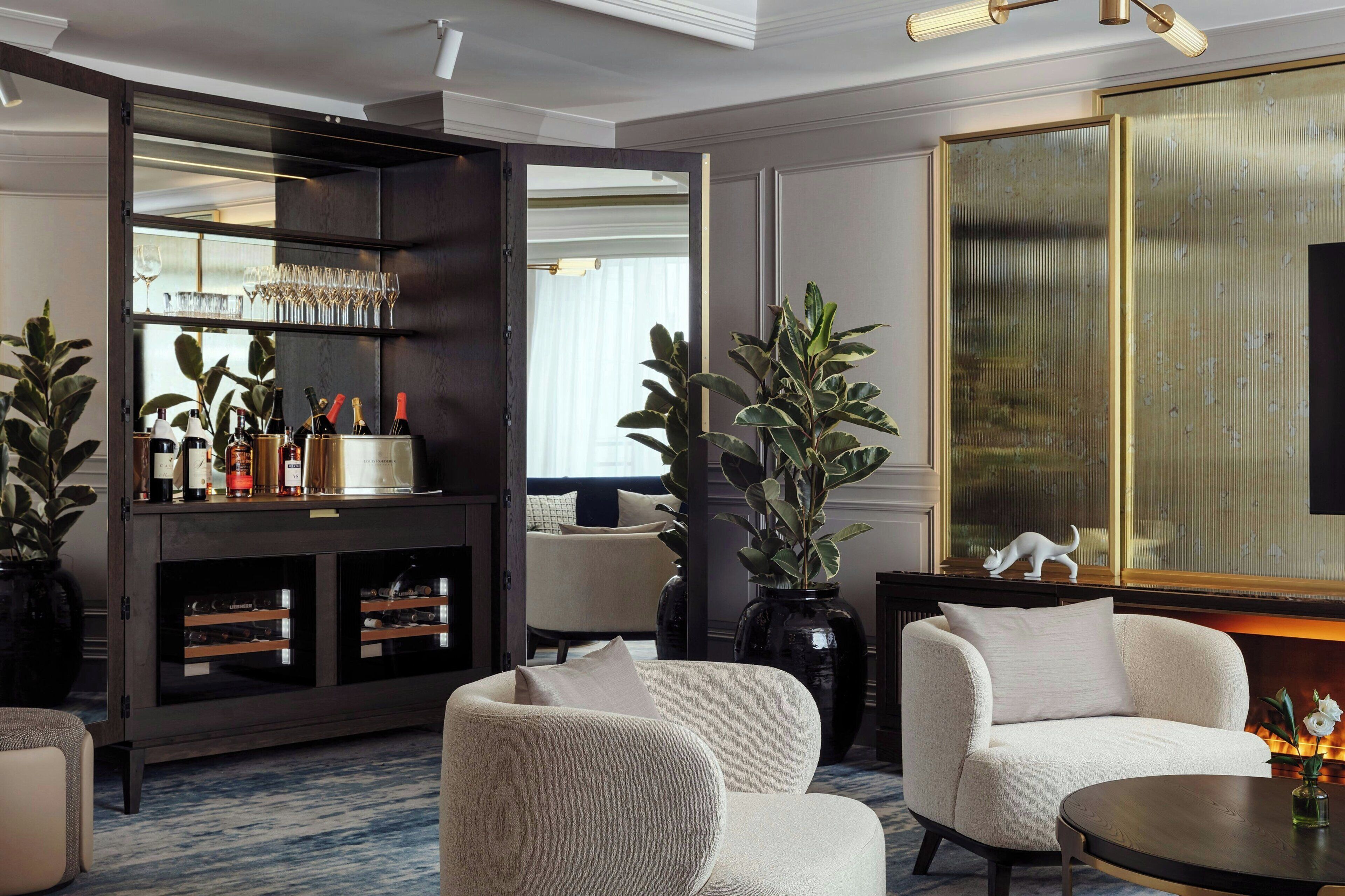 Un salon moderne avec un meuble en bois foncé contenant des bouteilles de vin et des verres, un canapé blanc et un grand miroir.