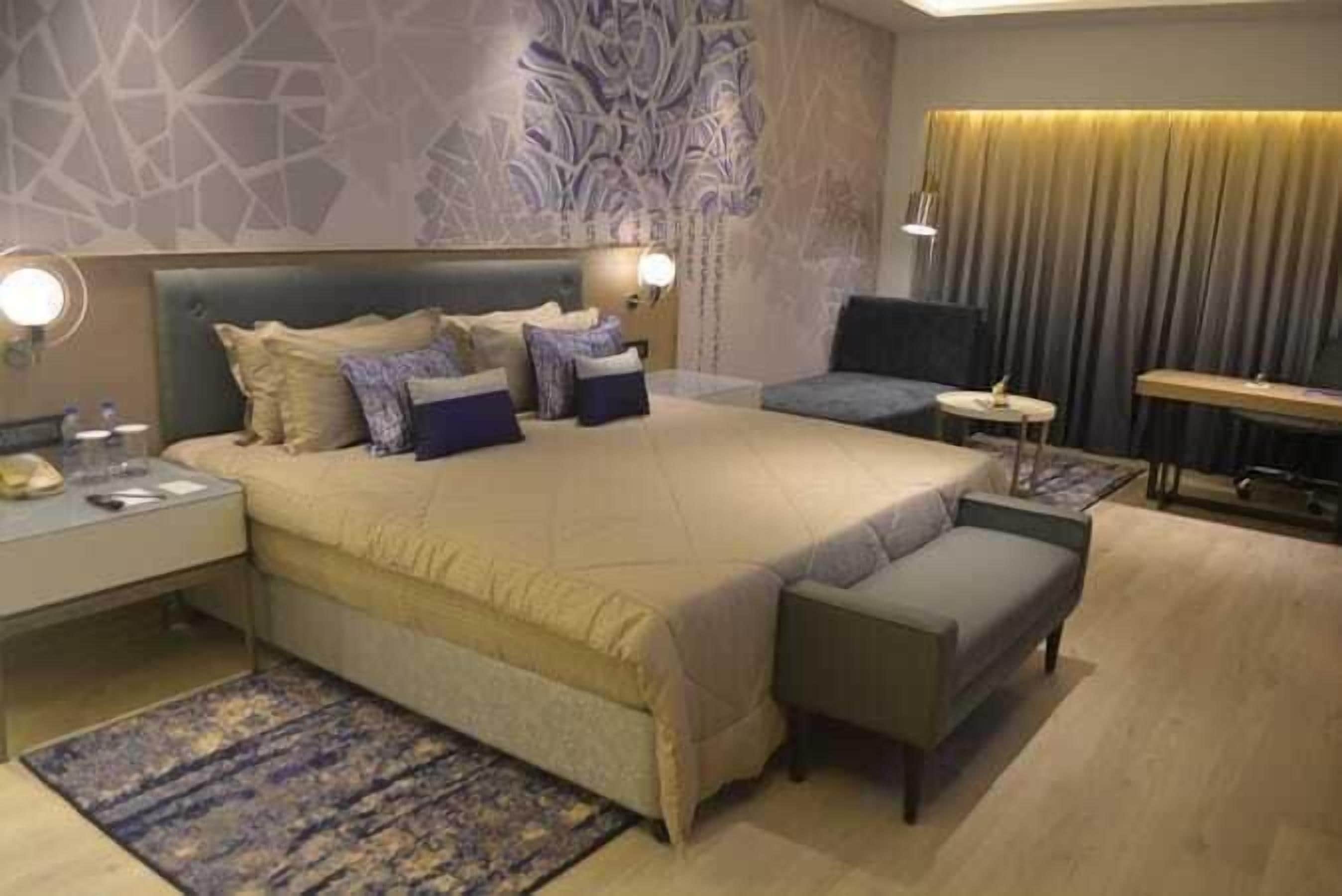 A modern hotel room with a large bed, a small sofa, a desk, and a chair.