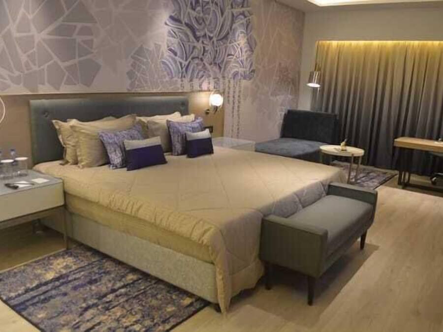 A modern hotel room with a large bed, a small sofa, a desk, and a chair.