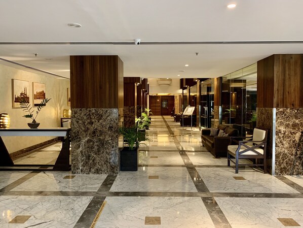 Un moderno hall de hotel con suelo de mármol, detalles de madera y una zona de estar con sofá y sillones.