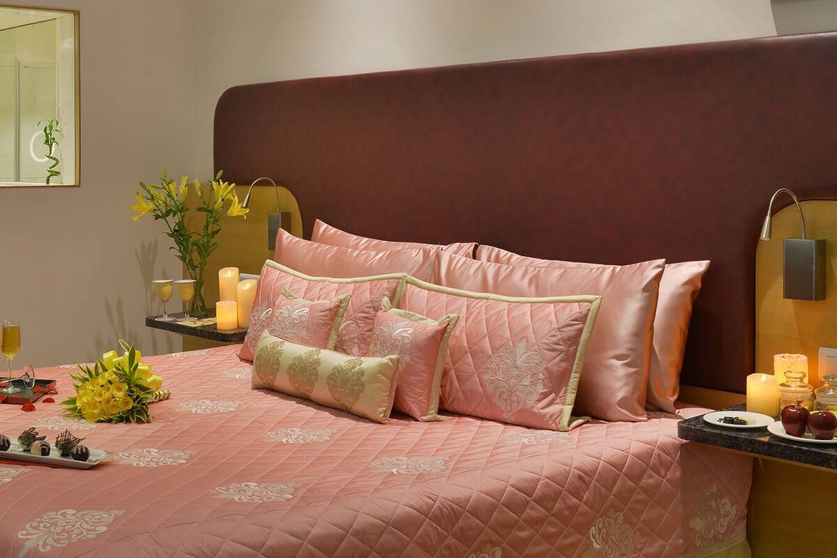 Une chambre à coucher bien rangée, avec un lit, des tables de chevet, un miroir et une petite table sur laquelle sont posées des bougies et une bouteille.