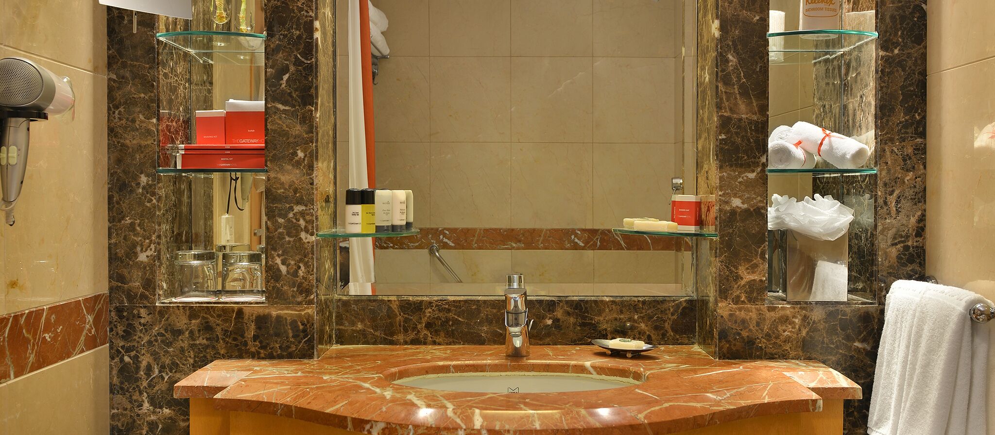 Une salle de bain avec un lavabo en marbre, des étagères en verre, un sèche-cheveux et des articles de toilette.