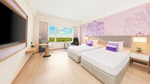 A hotel room with two beds, a desk, a chair, a TV, and a window with a view of greenery.