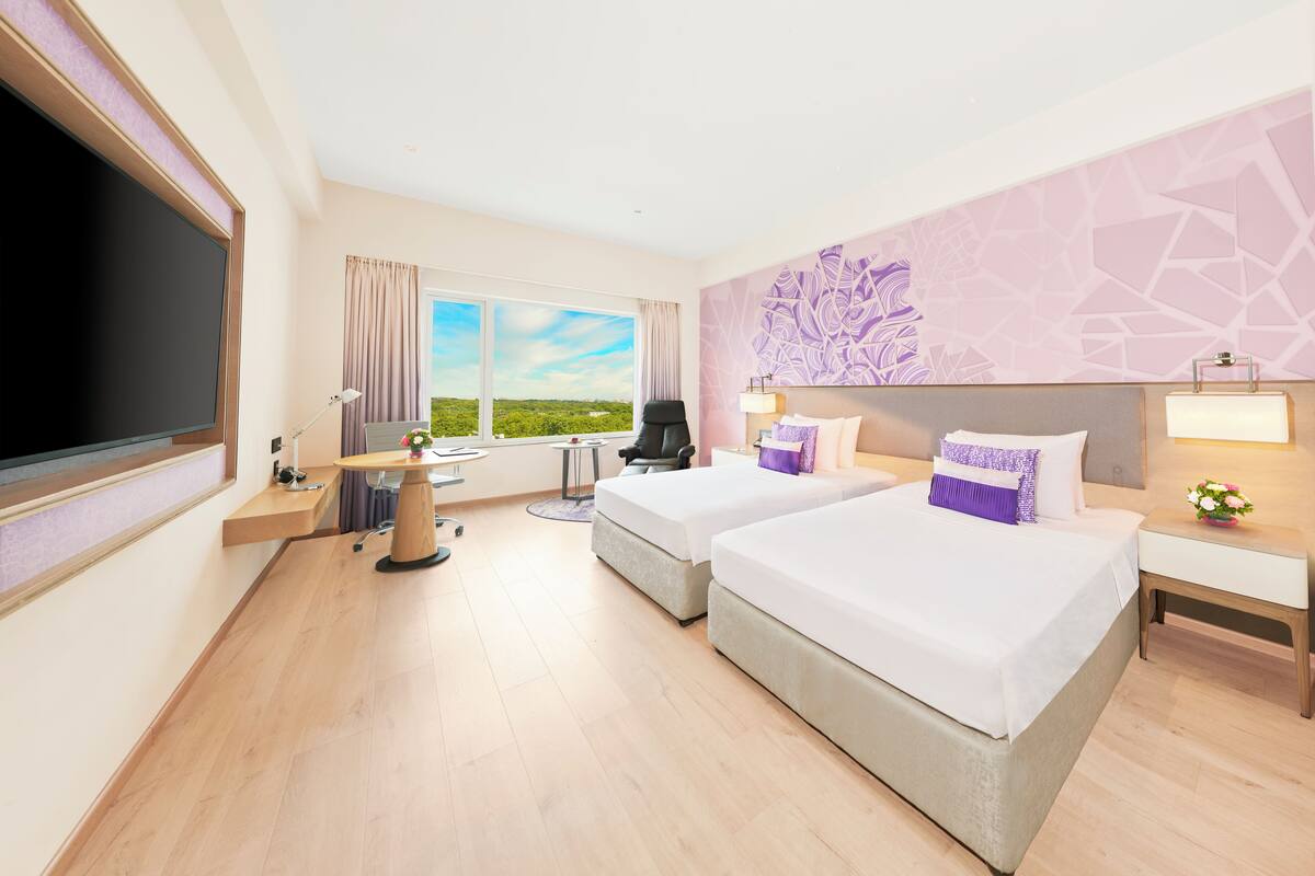 Une chambre d’hôtel avec deux lits, un bureau, une chaise, une télévision et une fenêtre donnant sur un paysage verdoyant.