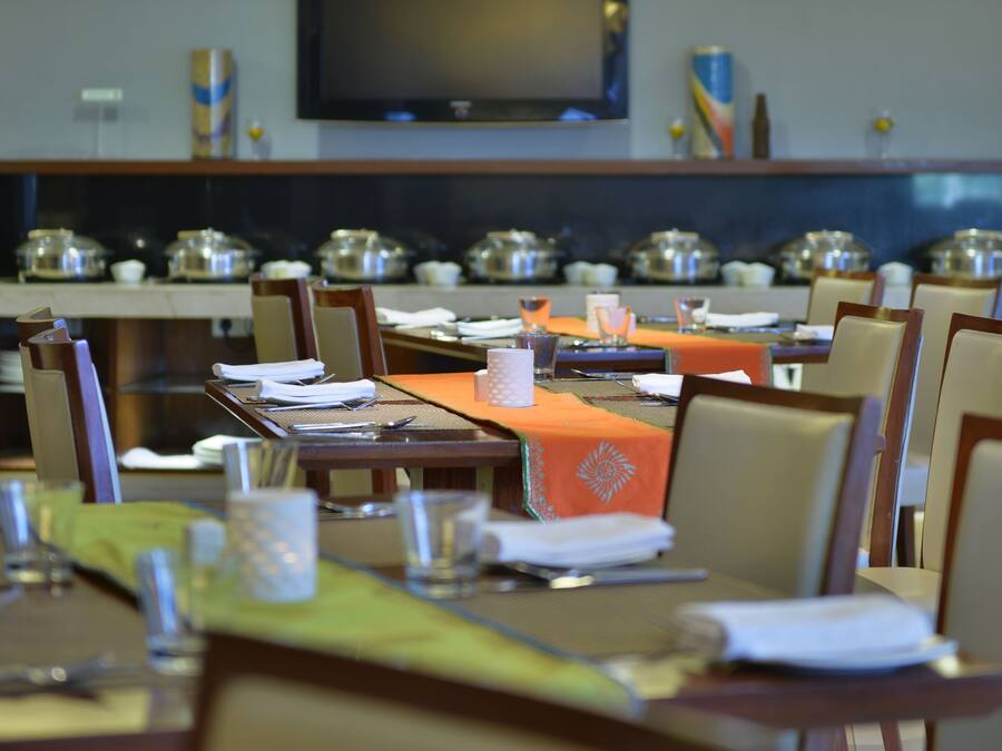 Un comedor con mesas dispuestas para comer, un televisor montado en la pared y servicio de buffet al fondo.